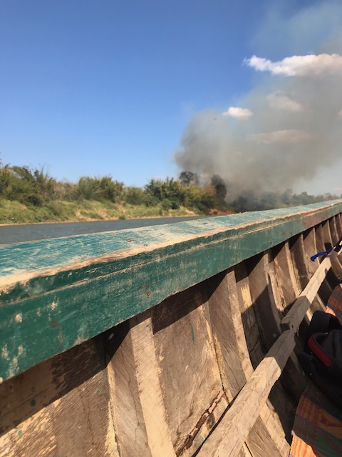 Smoke billows out from the forest next to the river as the malaria outreach team passes in a boat