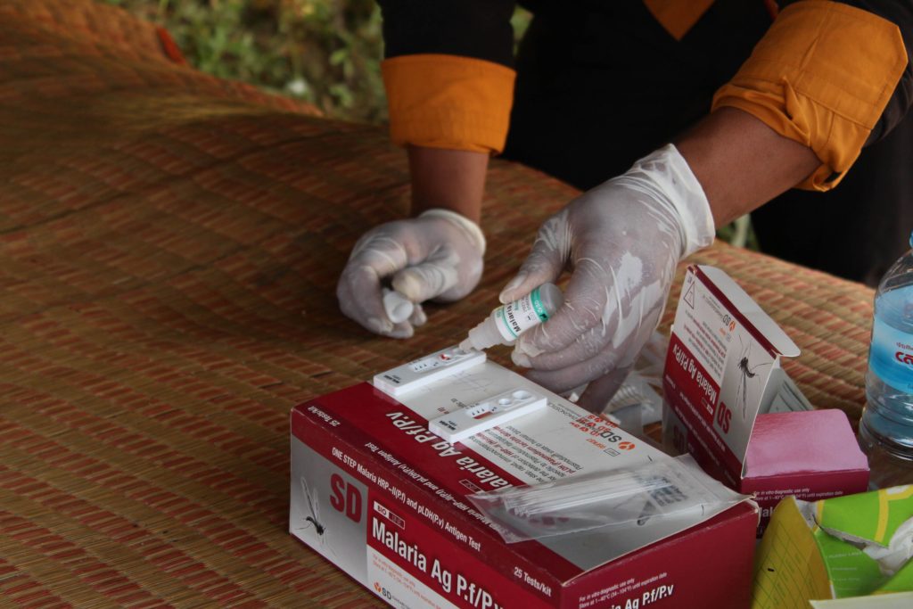 Blood samples are tested for malaria under the shade of a tarpaulin by a member of our outreach team