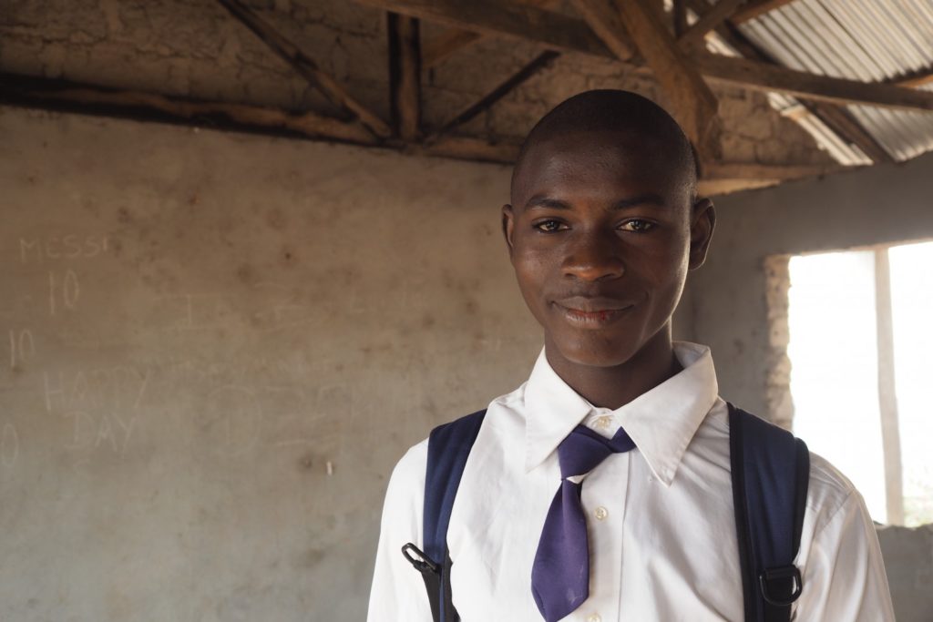 17 year old Augustine stands in his school classroom